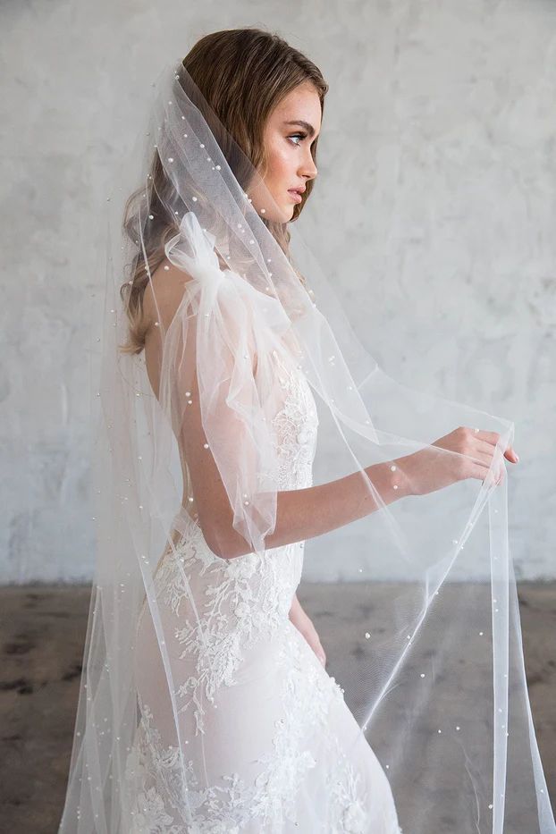 a woman in a wedding dress and veil is looking down at the floor with her hand on her hip