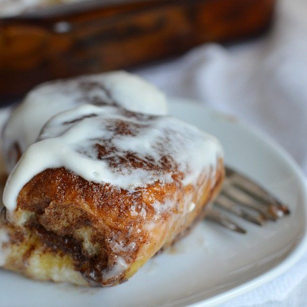 a piece of cinnamon roll with icing on a white plate next to a fork