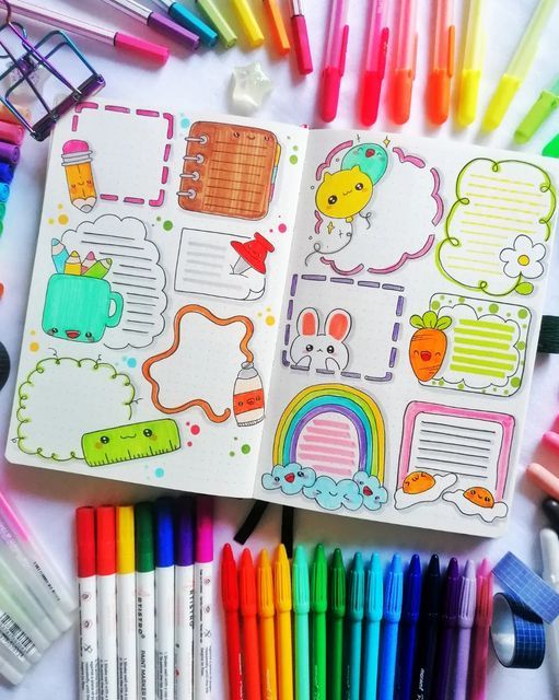 an open notebook with markers and pens on the table next to it is a bunch of different colored crayons