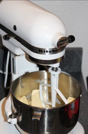 a white mixer sitting on top of a counter next to a metal bowl filled with batter