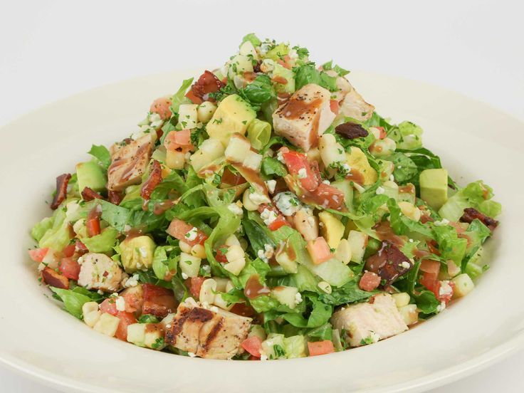 a salad with chicken, lettuce and tomatoes in a white bowl