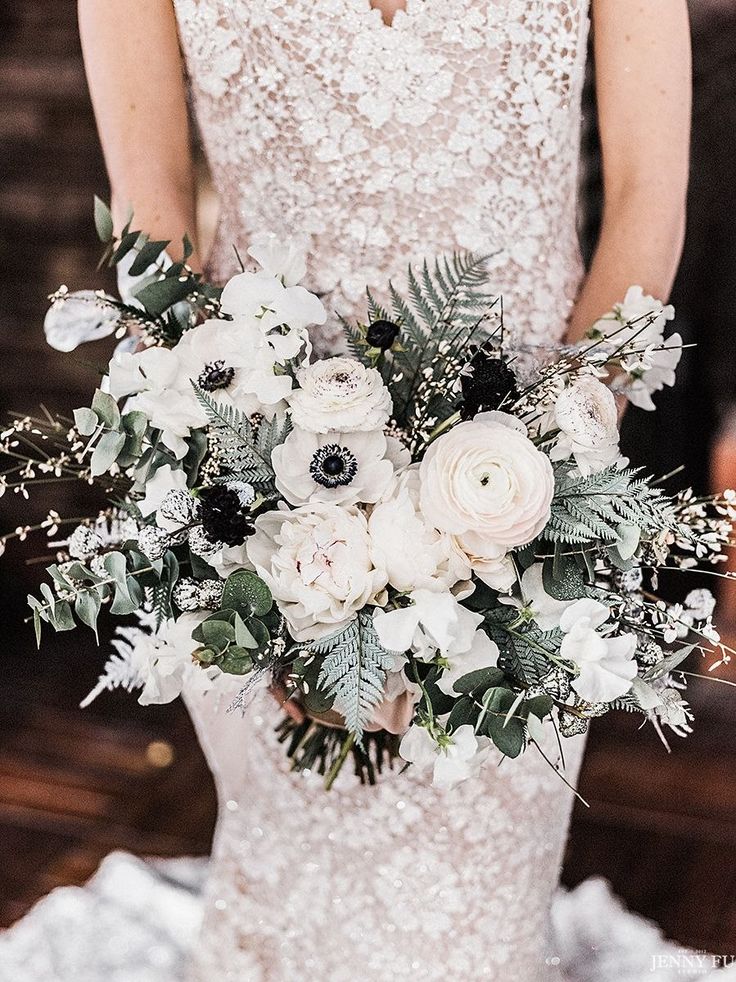 a woman in a wedding dress holding a bouquet of white and black flowers with greenery