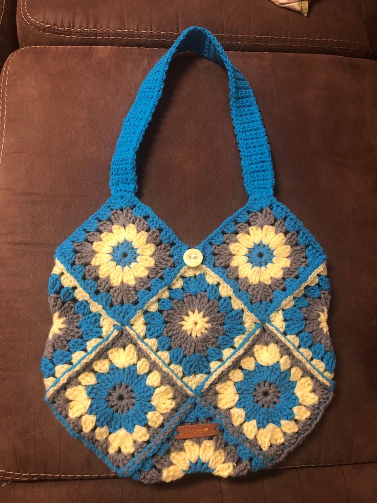 a crocheted blue and yellow purse sitting on top of a brown couch next to a remote control