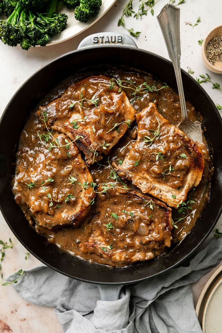 a skillet filled with meat and gravy next to some broccoli