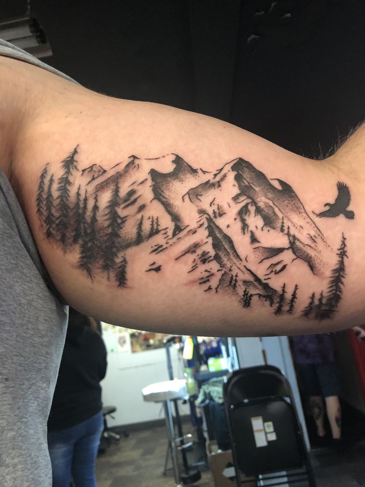 a man's arm with a mountain and pine trees tattoo on the upper half of his arm