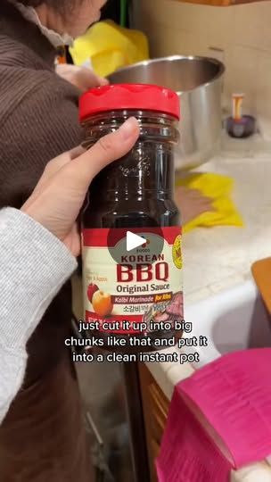 a person holding a jar of bbq sauce in front of a kitchen counter top