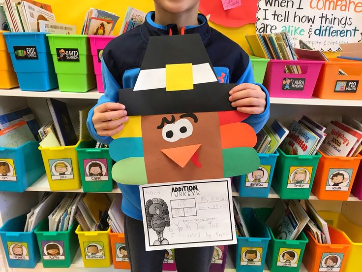 a young boy holding up a paper cut out of a turkey in front of bookshelves