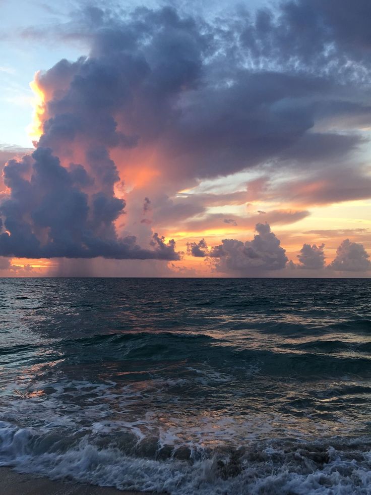 the sun is setting over the ocean with clouds in the sky and waves on the beach