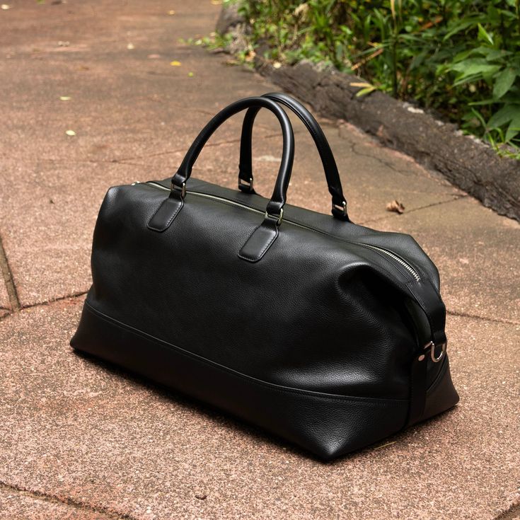 A Duffel Bag in Black Pebble Grain Leather for the weekend or overnight travel. Designed with top handles and a double zipper closure.  Product Details: Designed in soft, full grain cowhide leather with an embossed pebbled texture, making it resistant to everyday wear and tear Interior is lined with fabric in black. Fabric is made from cotton-polyester blend, that is very breathable. The duffel bag has a top zip closure and leather handles for easy carry Two YKK metallic zippers that ensure a lo Luxury Black Soft Leather Weekender Bag, Black Leather Duffle Bag With Smooth Grain, Black Textured Leather Duffle Bag For Everyday, Black Duffle Bag With Smooth Grain For Everyday Use, Black Rectangular Duffle Bag With Smooth Finish, Black Smooth Grain Duffle Bag For Everyday Use, Classic Black Travel Bag With Smooth Grain, Classic Black Textured Leather Duffle Bag, Classic Black Textured Leather Travel Bag