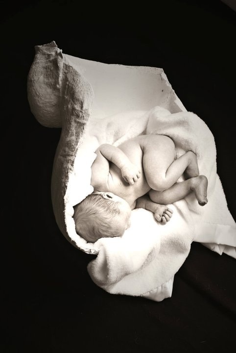 a black and white photo of a baby wrapped in a blanket on top of a pillow