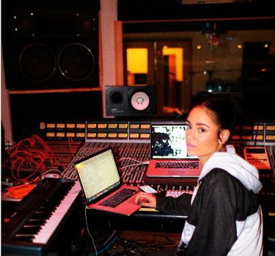 a woman sitting in front of a laptop computer on top of a desk next to sound mixing equipment