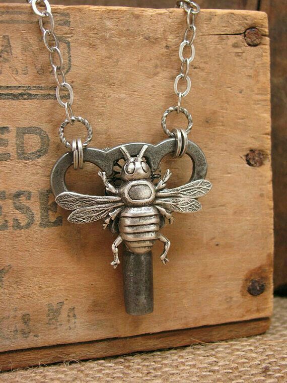 a metal key with a bee on it is sitting on a wooden box and has a chain attached to it