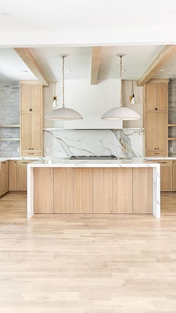 an empty kitchen with marble counter tops and wooden cabinets, along with two pendant lights hanging from the ceiling