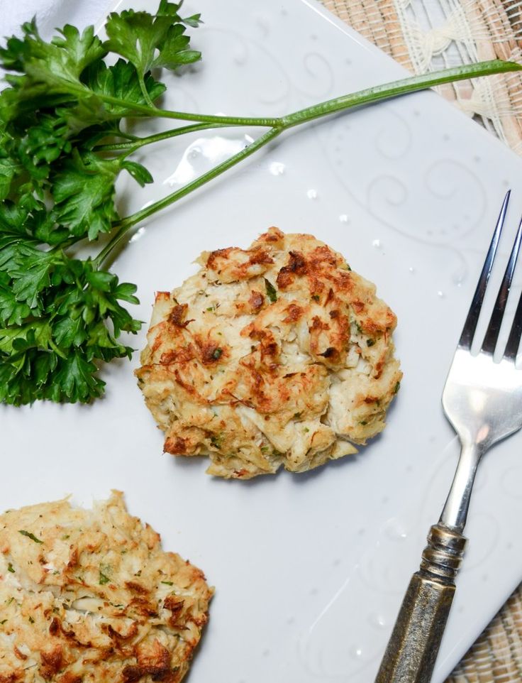 two crab cakes on a white plate with a fork and parsley next to it