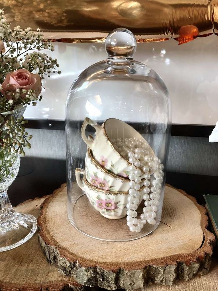 a glass clochet with some teacups under it on top of a tree stump