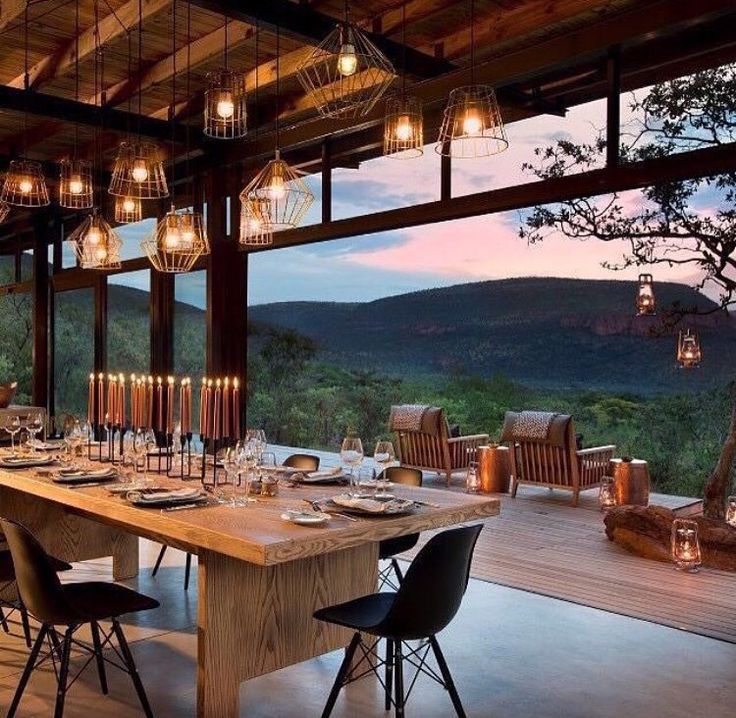 an outdoor dining area with wooden tables and chairs, overlooking the valley outside at dusk