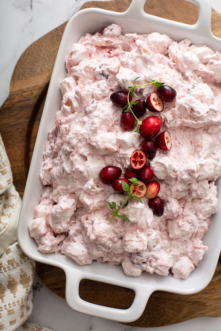 a dish filled with cranberry salad on top of a wooden cutting board next to a white towel