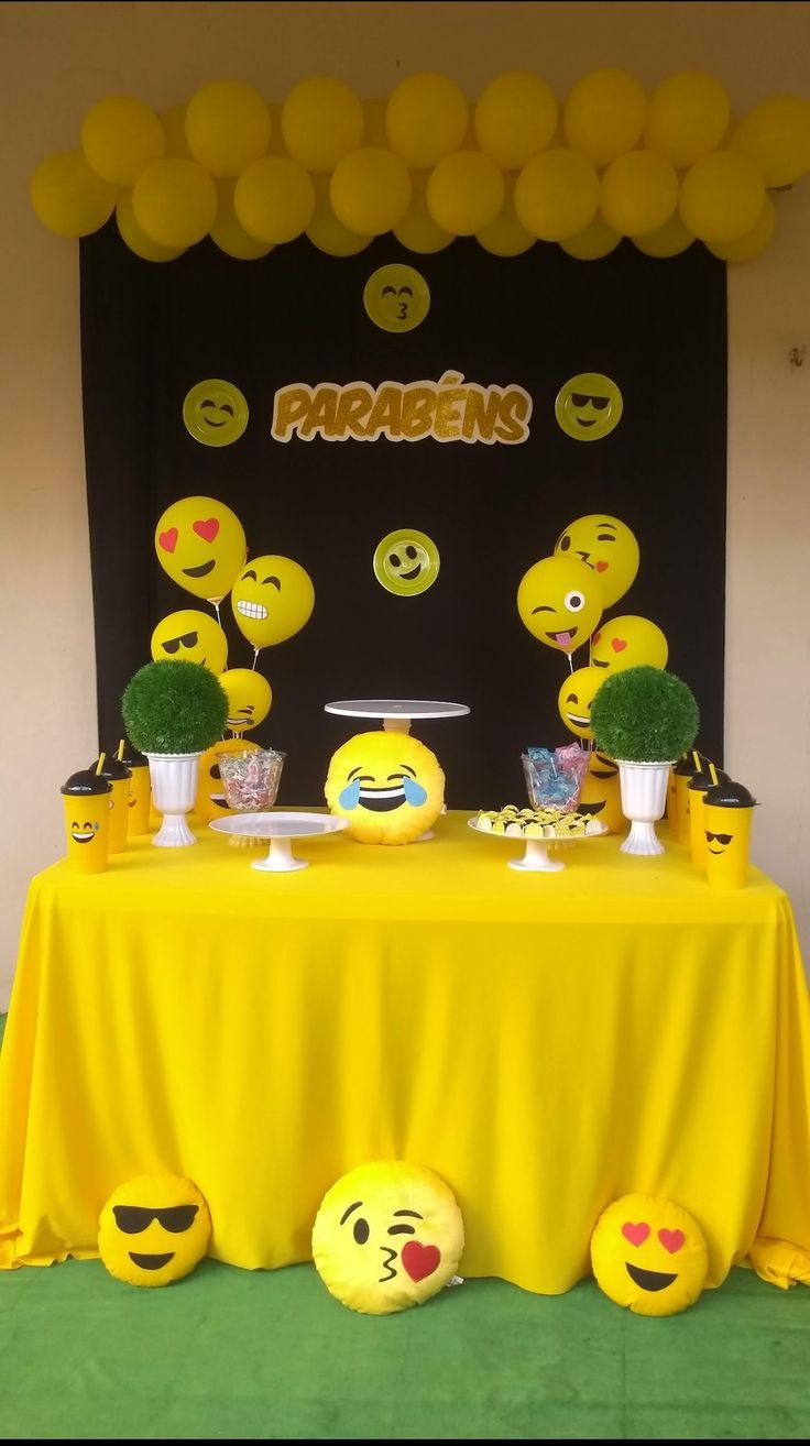 a table topped with lots of yellow balloons and emoticting faces on top of it