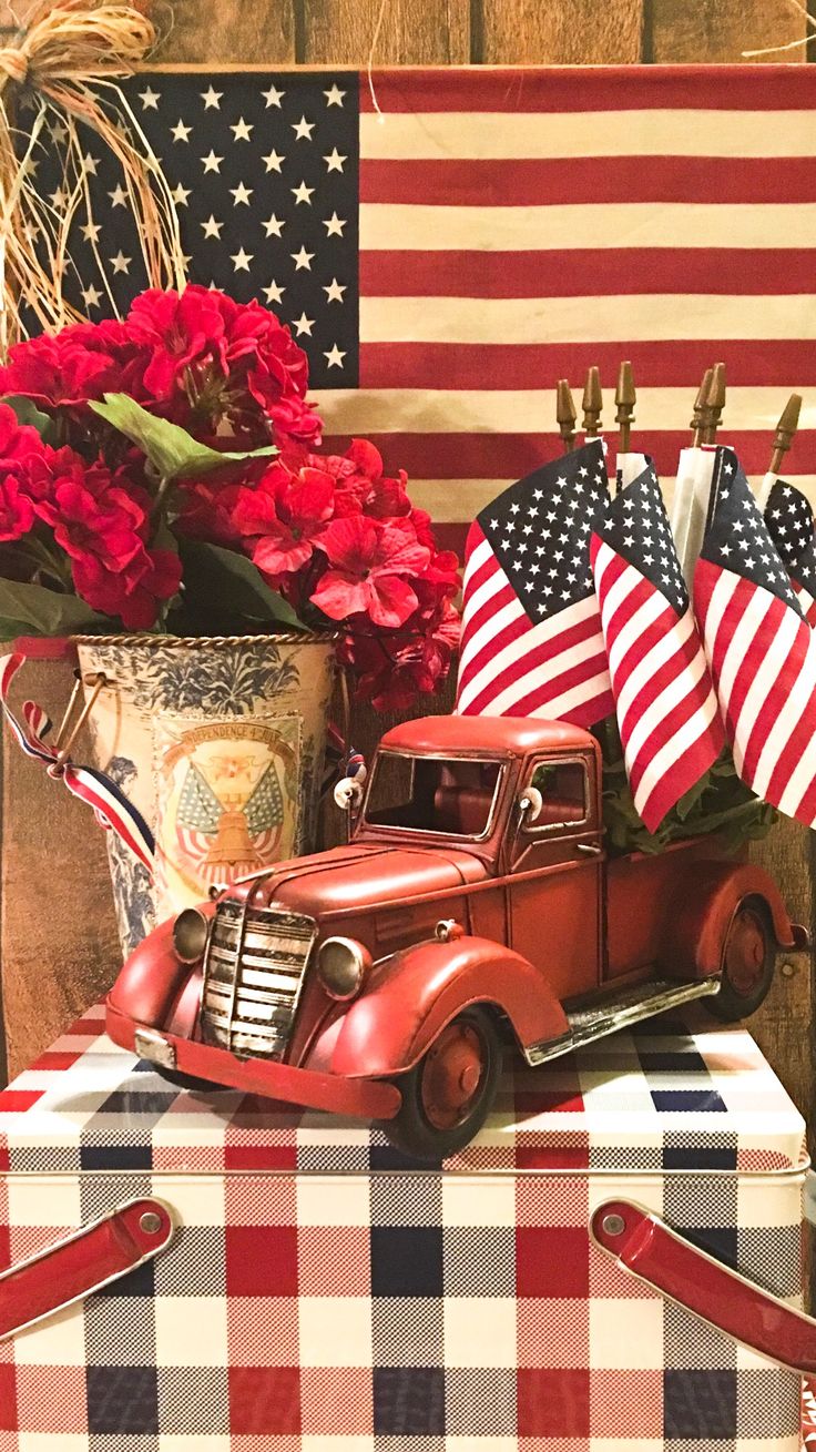 an old red truck with american flags and flowers in the back sits on a checkered table cloth