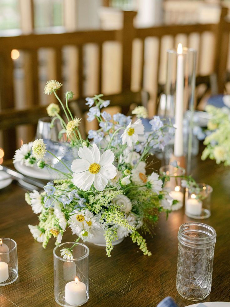 a wooden table topped with vases filled with white flowers and lit votive candles