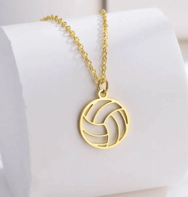 a gold necklace with a volleyball ball on it's chain, sitting on top of a white napkin