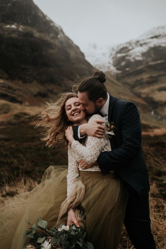 a man and woman hugging each other in the middle of a field with mountains behind them