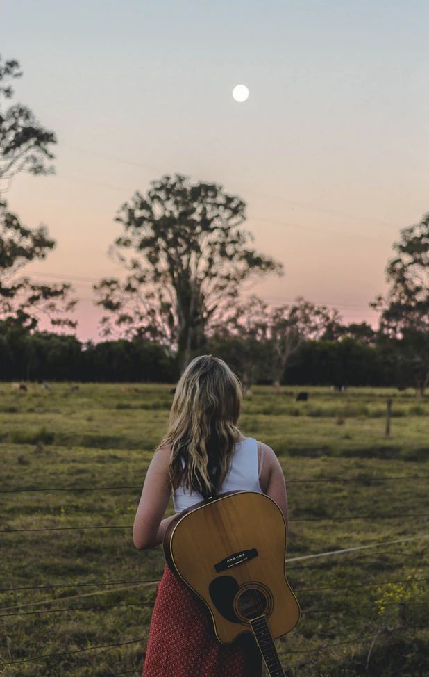 a woman in a red dress is holding an acoustic guitar and looking at the sky