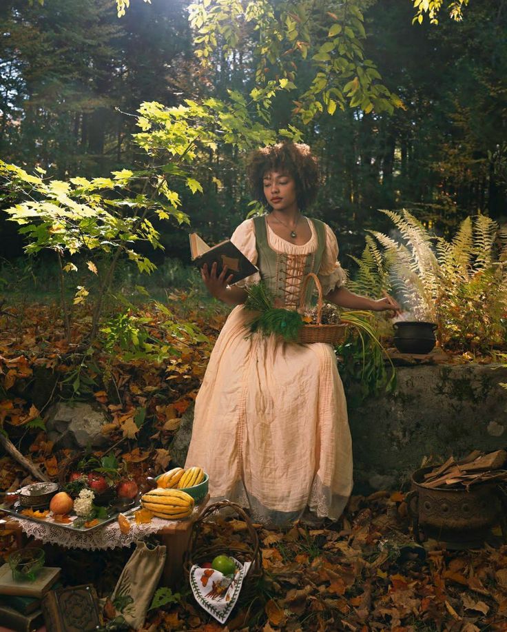 a woman dressed in an old fashioned dress sitting on the ground surrounded by autumn leaves