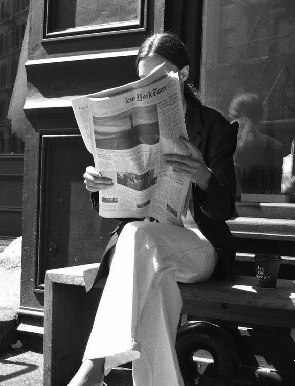 a woman sitting on a bench reading a newspaper