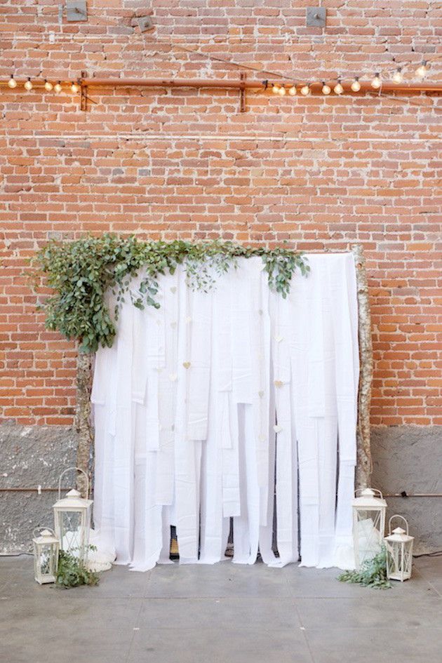 an outdoor wedding ceremony with white drapes and greenery on the side of the building