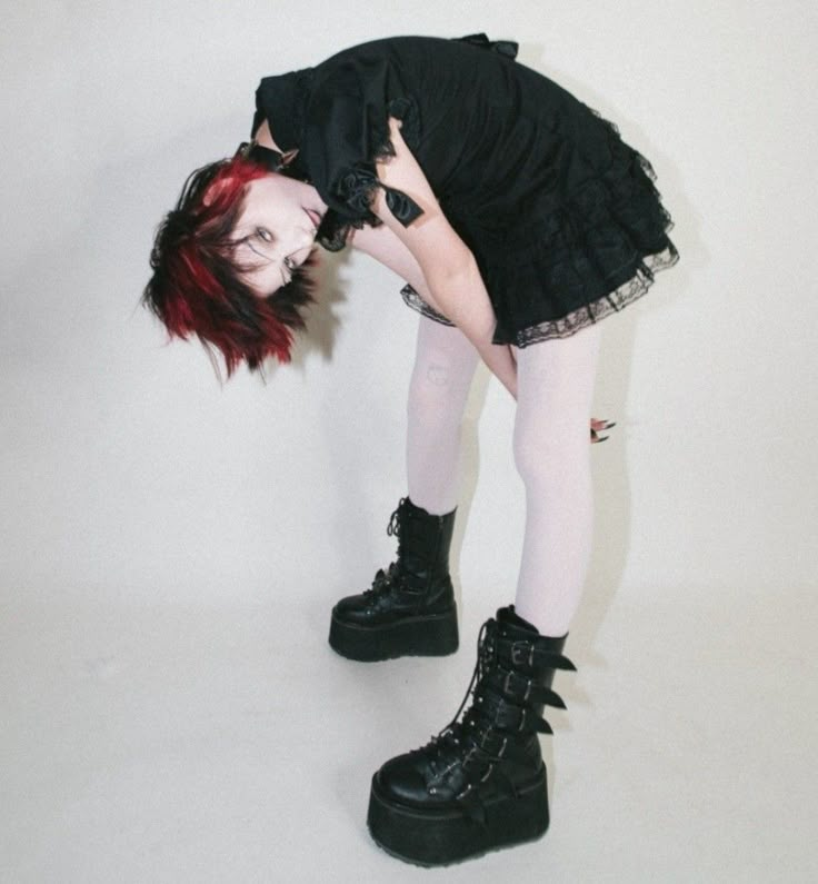 a woman with red hair and black boots is bent over on her knees while wearing all black