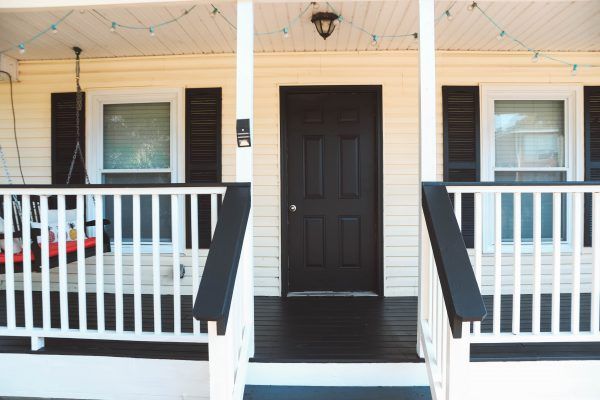 the front porch of a white house with black doors and railings on both sides