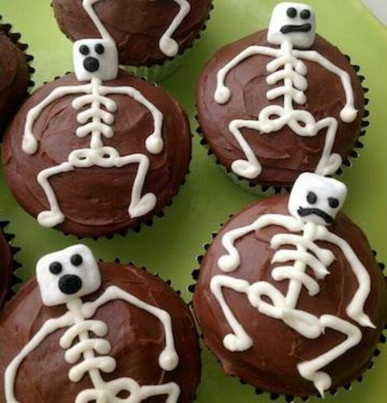 chocolate cupcakes decorated to look like skeletons with white icing on them, sitting on a green plate