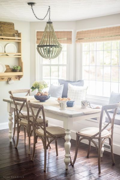 a dining room table with four chairs and a bench in front of two windows that have roman shades on them