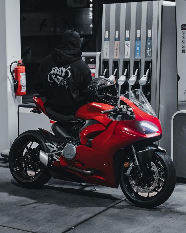 a red motorcycle is parked in front of a gas station with a man on it