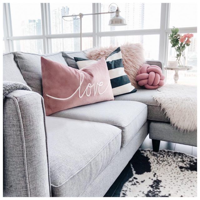 a couch with pillows on top of it in front of a window and a rug