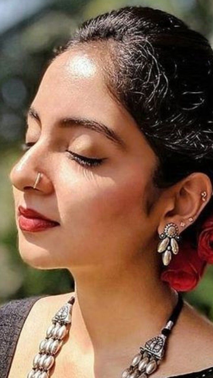 a woman with her eyes closed wearing some earrings and a red rose in her hair