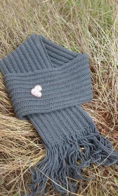 a gray knitted scarf laying on the ground next to some brown and green grass