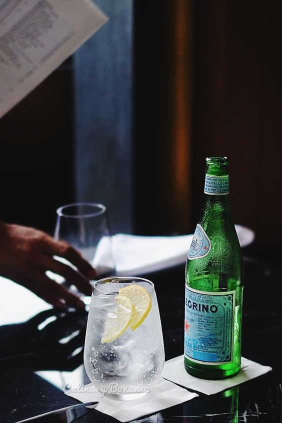 a bottle of gino next to a glass filled with ice and lemon wedges