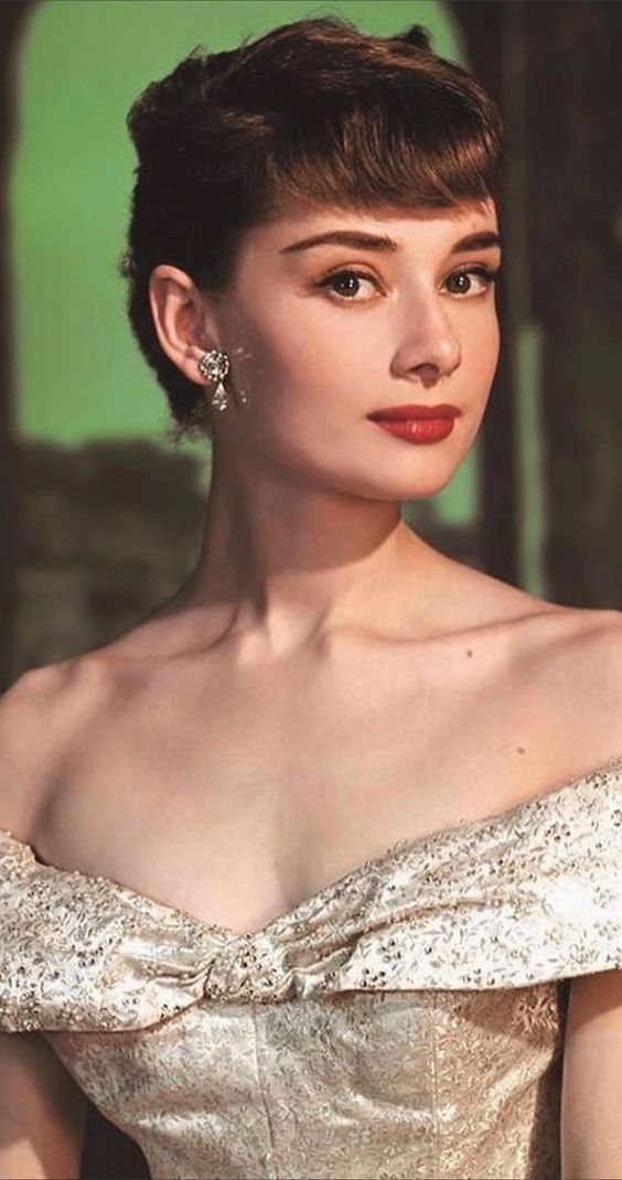 a woman with short hair wearing a white dress and diamond earrings, posing for the camera