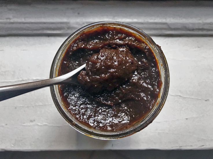 a spoon in a jar filled with brown sauce on top of a white countertop