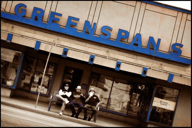 two people sitting on a bench in front of a building with the words greenspans painted on it