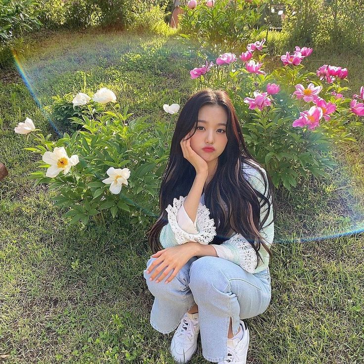 a woman sitting on the ground in front of flowers with her hand under her chin