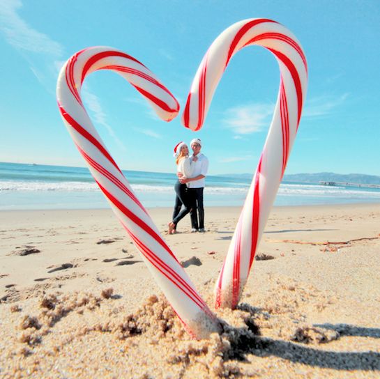 two people standing on the beach with candy canes in the shape of a heart