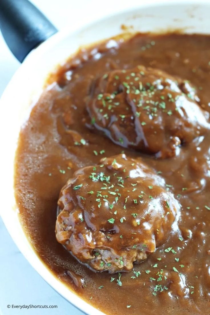 two meatballs covered in gravy and garnished with green sprinkles