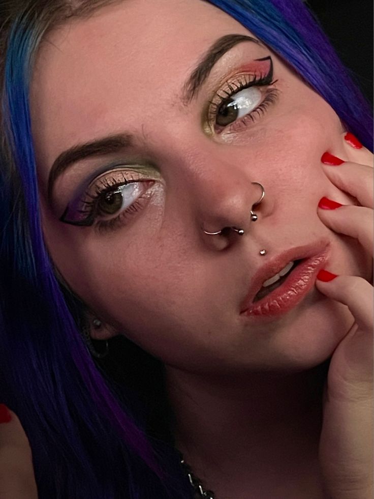 a woman with blue hair and piercings on her nose is posing for the camera