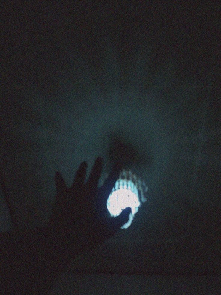 a person holding their hand up in the dark with a light shining on them behind him