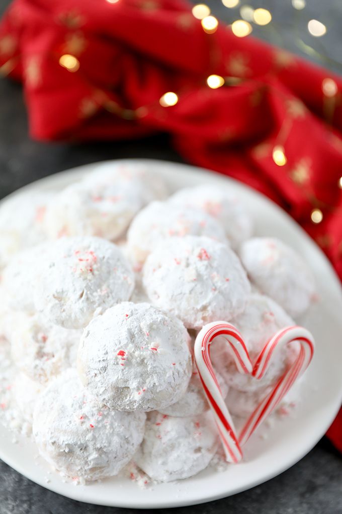 a white plate topped with snowball cookies next to a red bow and candy cane