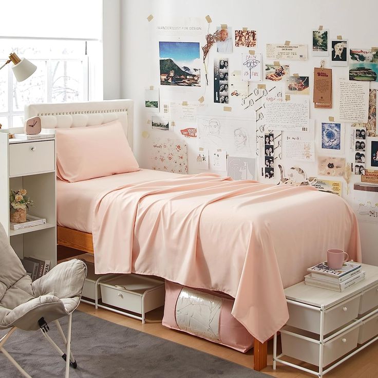 a bedroom with pink sheets and pictures on the wall above the bed, along with a chair