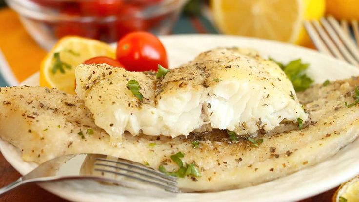 a white plate topped with fish next to lemons and tomatoes